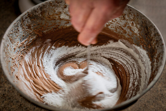 Close Up Of A Hand Mixing Sugar And Chocolate Cake Batter In A Bowl.