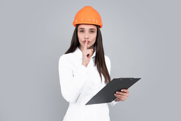Serious woman in protective helmet with clipboard isolated on grey background. Young woman construction manager. Architect woman, female worker in hardhat helmet.