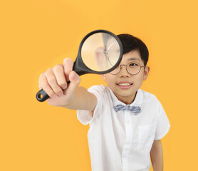 Exploration concept with little student in bow tie and glasses having fun watching and observing with magnifying glass

