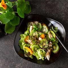 plate with salad with chicken breast, kiwi and tomatoes on a dark table