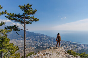 A happy woman stands on top of a mountain and looks at the sea and the city in the distance