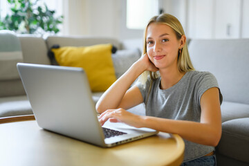 Happy teenager girl online with a laptop in the living room at home