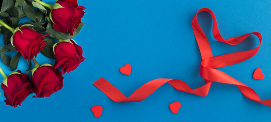Red heart shaped ribbon and red roses on the blue background. Top view. Copy space.