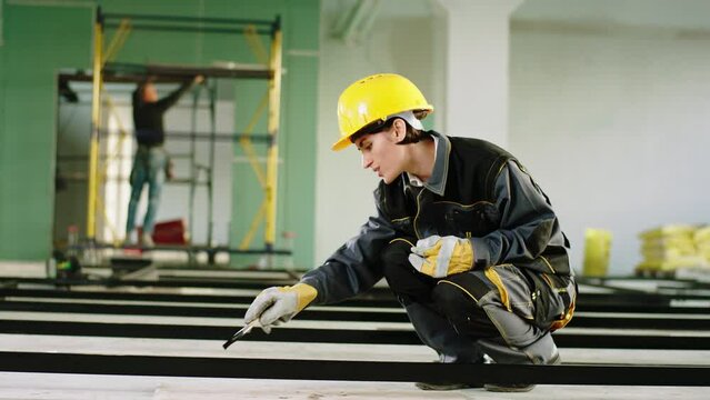 Large spacious building in construction working concentrated charismatic woman constructor worker using a brush to painting the building materials she wearing safety helmet and special uniform