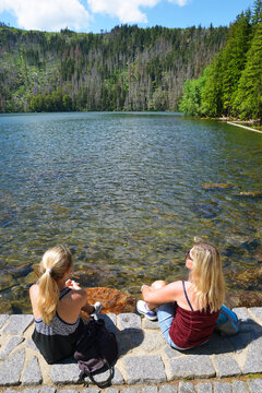 Two women sitting by Black lake (Cerne jezero) in the National park Sumava, Czech Republic.
