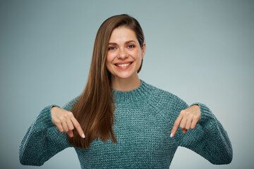 Smiling woman in green sweater pointing fingers down at copy space. Advertising female studio...