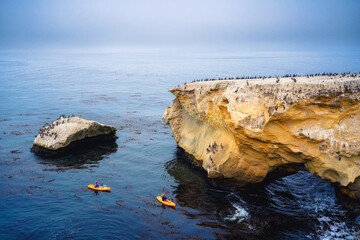 Ocean kayaking. People paddling kayaks overlooking Pacific ocean, rocky cliffs and caves close to Shell Beach, California