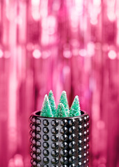 A forest of miniature Christmas trees sits in a decorative glass container against a backdrop of red glittery tinsel. Simple modern template with copy space for new year greeting card, banner.