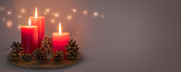 three red burning candlelights with pine cones on grey background with copy space, bright illumination for christmas decoration in contemplative atmosphere at night