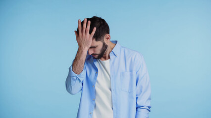 displeased bearded man in shirt touching head with hand isolated on blue