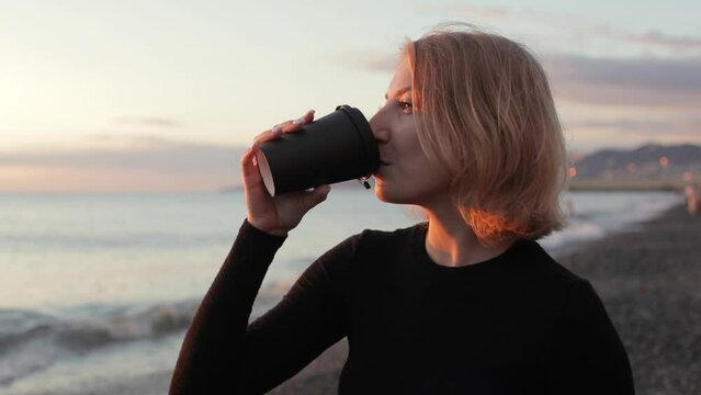Beautiful woman relaxing and drinking coffee against the sea at sunset.
