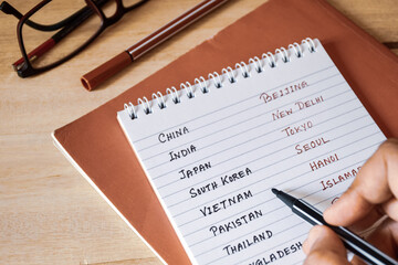 Asian country names with their capitals on notepad. Student's  preparation for competitive exam concept.