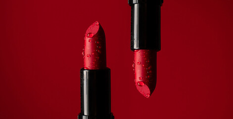 close-up on two red lipsticks in splashes of water on a red background