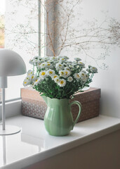 Bouquet of chrysanthemums in a vintage ceramic mug, a craft box, a lamp on the windowsill . Cozy home interior