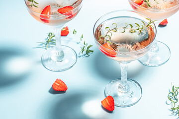 Glasses with cold pink champagne or punch with wine strawberries, ice and rosemary on blue background