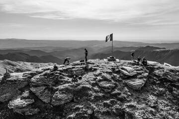 Black and white shot of group of hikers near the flag on the top of rocky mountain