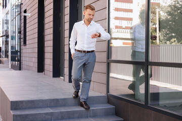 portrait of a man in a shirt walks and looks at his watch near the building