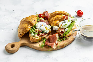 Croissant with prosciutto, poached egg, jamon, blue, cheese, avocado, microgin and cherry tomatoes. Mediterranean appetizer. Breakfast concept