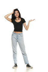 Young excited woman in jeans and shirt, advetising product on her palm,  front view on a white background