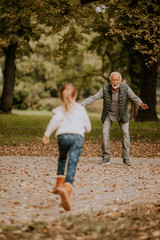 Grandfather spending time with his granddaughter in park on autumn day