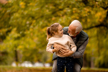 Grandfather spending time with his granddaughter in park on autumn day