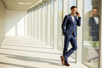 Young business man using mobile phone in the modern office hallway