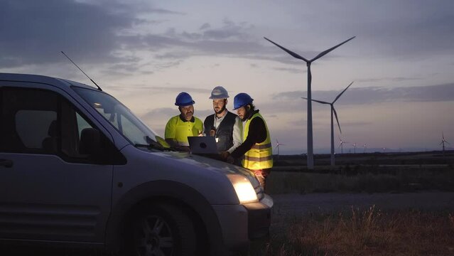 Group of engineers in discussed the plan for the maintenance of wind turbines working with a laptop in a field wind turbines power station. Renewable and clean energy concept, sustainable future
