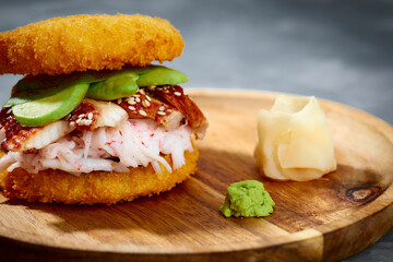 Pan-Asian cuisine concept. Japanese sushi burger made from rice bread, crab meat, avokado and wasabi sauce. Serving on wooden board. copy space
