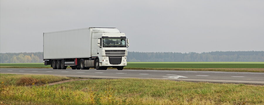 White semi truck move on countryside motorway road on green field . Front side view . Long hauls ransportation logistics