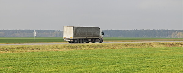 Heavy gray semi truck van drive on countryside highway road on green field . Back side view ....