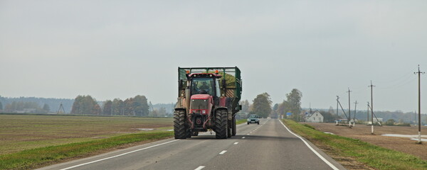 Big red wheeled tractor with heavy trailer on countryside highway road on field