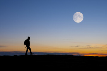 Hiker walking under the full moon at dusk.