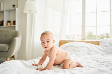 Cute baby in a diaper on the bed in the bedroom.