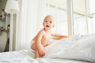 A cute baby in a diaper takes the first steps in bed.