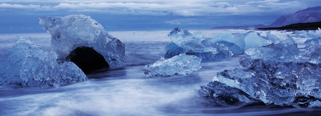 Ocean water washes over pieces of floating ice as sea spray fills the cold Icelandic air in this...
