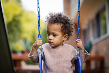 Biracial toddler plays on blue swings in backyard in fall
