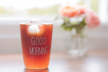 Iced coffee in a clear glass in the morning with natural light by the window. Green nature background and sweet pink roses, Healthy drink concept, Kombucha americano, Fermented tea with probiotics.