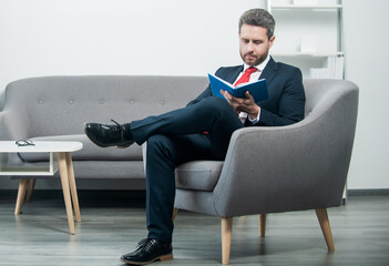 mature businessman in suit sit in office read book