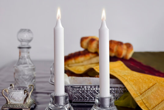 2 Shabbat candles on a Shabbat table with homemade challah and a Kiddush cup in the background
,candles and wine for Shabbat, shabbatchallah bread and candles on wooden table'Shabbat Shalom