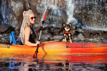 Happy young woman with her chihuahua dog paddling against waterfall background - obrazy, fototapety, plakaty