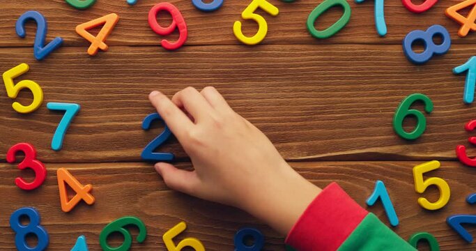 Child hand puts colored numbers 2023 new year on wooden background