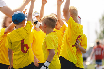 Happy kids sports team stacking hands at the field. Motivated children sports team rising hands....