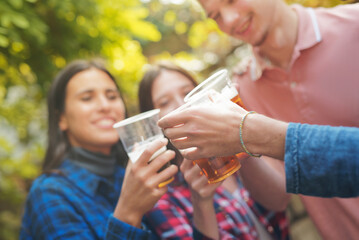 Group of four young friends cheering with beer in plastic glasses, celebrating their friendship, autumn surrounding