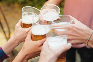 Group of four young friends cheering with beer in plastic glasses, celebrating their friendship,...
