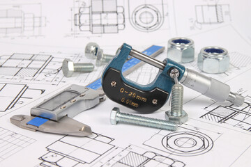 micrometer, caliper and hardware on a background of engineering drawings. Science, mechanics and mechanical engineering.