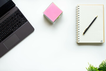 Modern workspace on a white desk table with laptop, keyboard and other office supplies. Blank notebook page for input text. Still life workplace top view, flat lay with copy space.