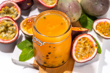 Homemade passion fruit jam in small jar, with fresh passion fruit and mint leaves on white kitchen background copy space
