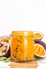 Homemade passion fruit jam in small jar, with fresh passion fruit and mint leaves on white kitchen background copy space