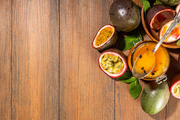 Homemade passion fruit jam in small jar, with fresh passion fruit and mint leaves on wooden background copy space