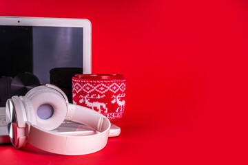 Festive red composition with white laptop computer, headphones, big cup for hot chocolate. Christmas mood and vibe, listen traditional new year songs music. Preparation for Christmas background